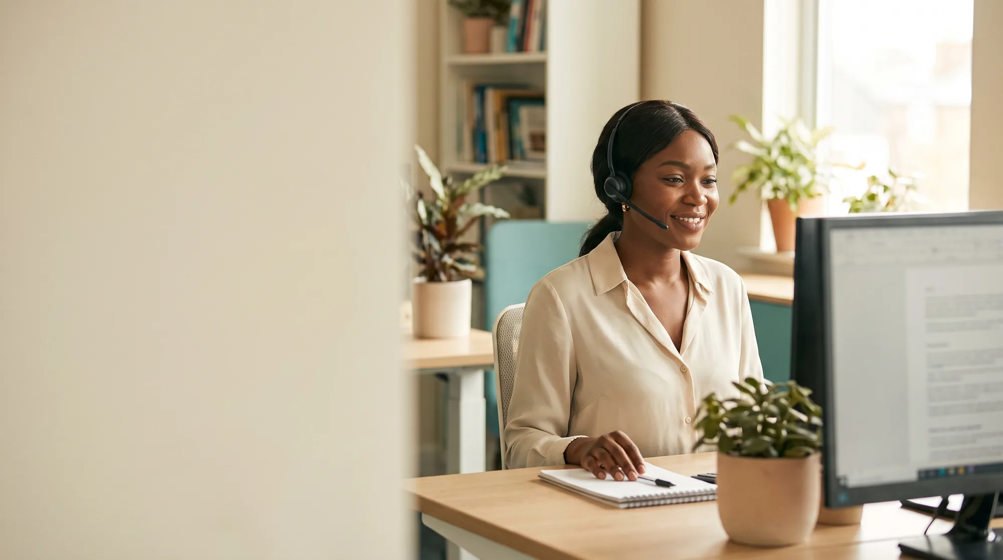 A care coordinator with a headset answers WhatsApp messages with a soft smile.
