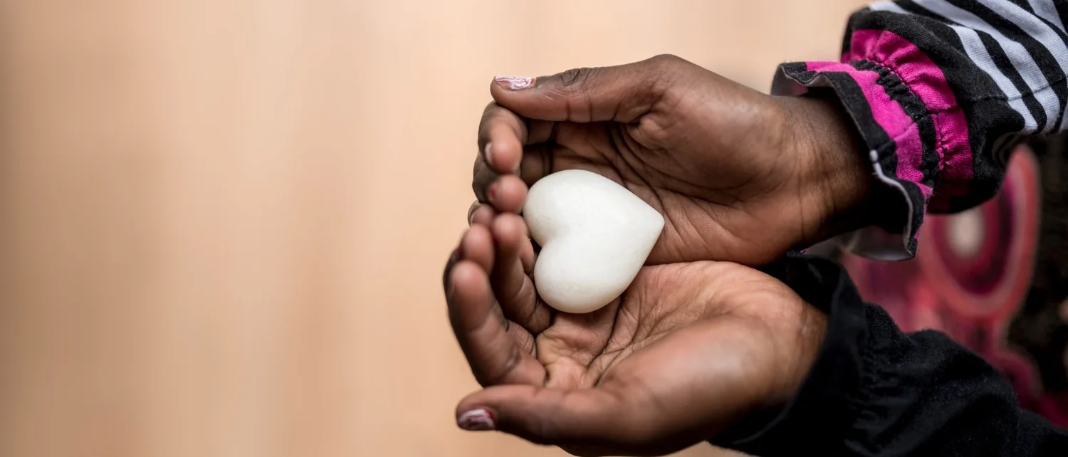 A pair of young hands cradling a heart-shaped stone, care held carefully.